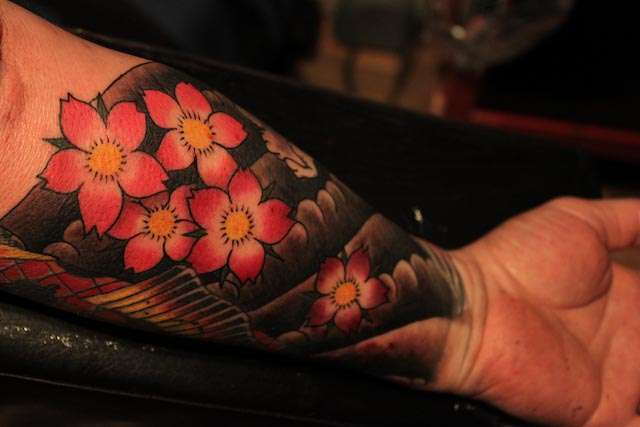 Tatuaje flores de cerezo sobre fondo negro en antebrazo